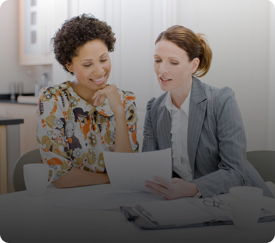 Two women discussing documents in office setting.