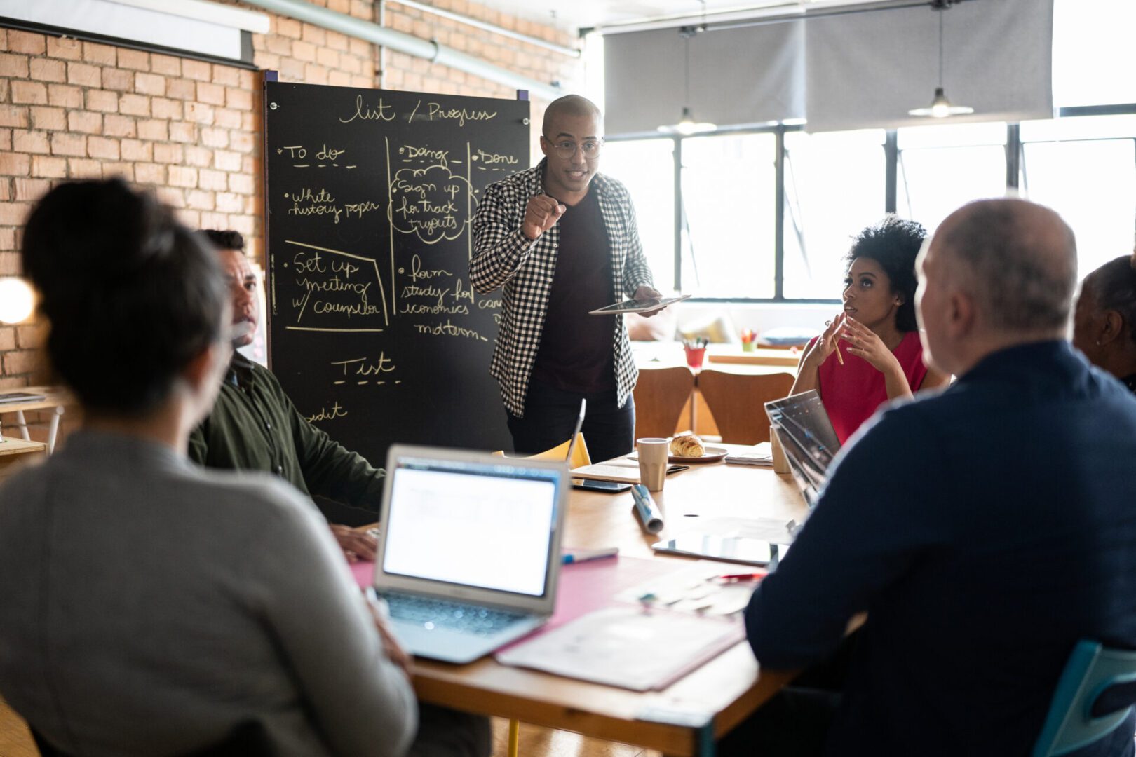 Team discussing ideas around a table with a blackboard in the background.