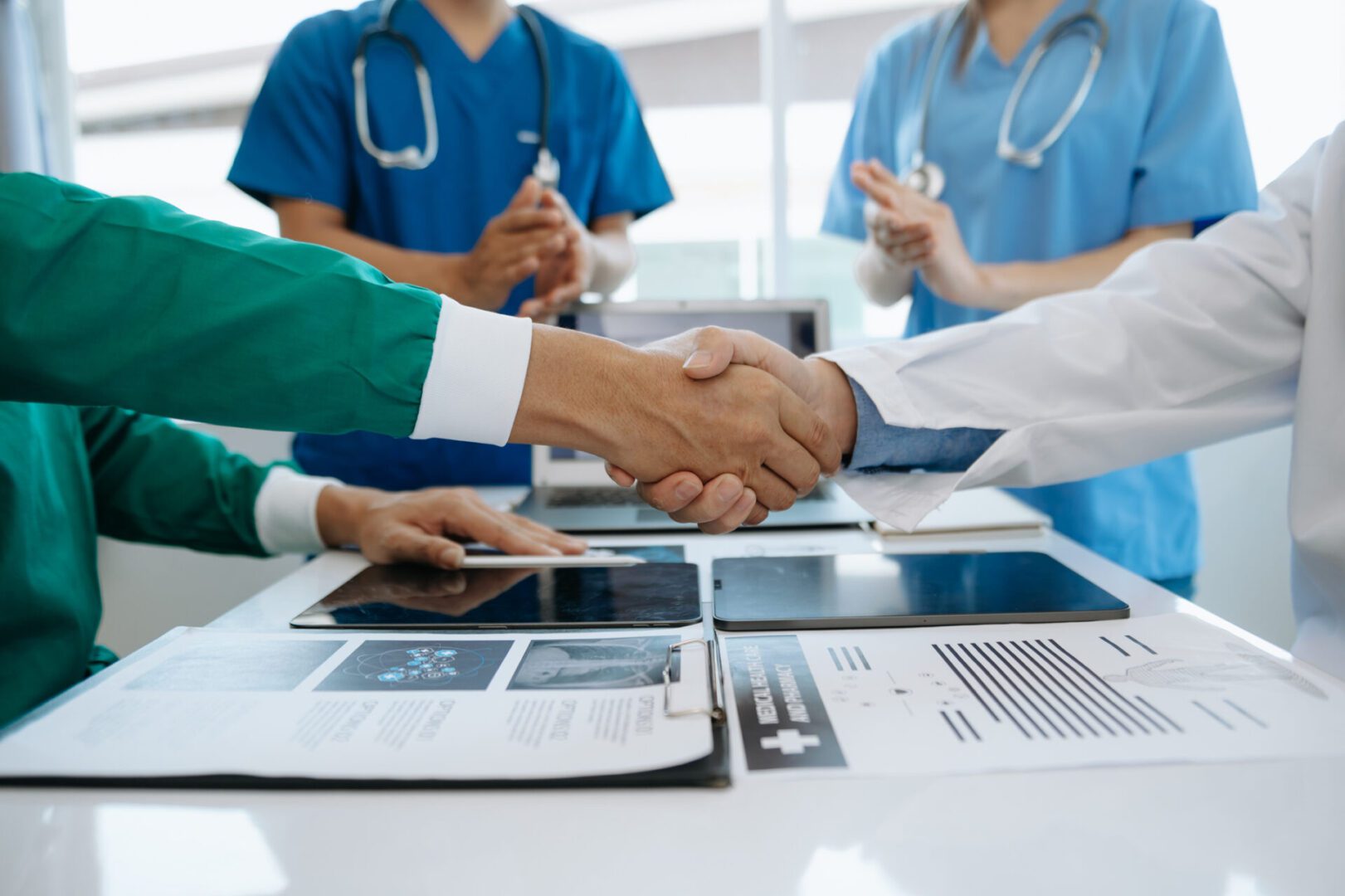 Doctors shaking hands over patient X-rays during a meeting.